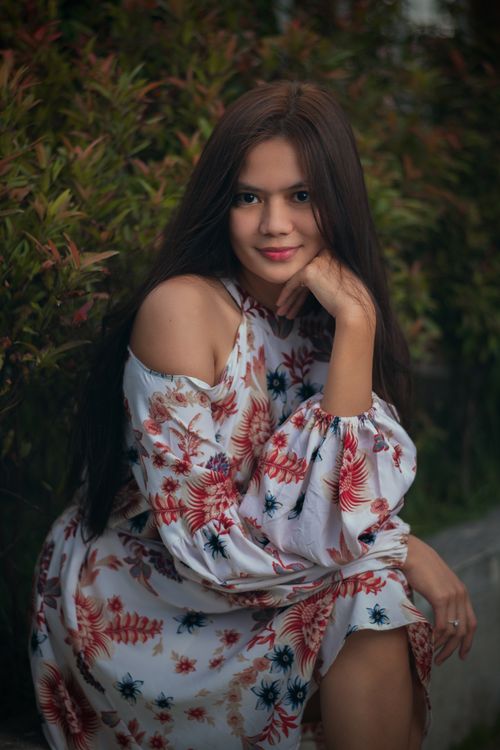 Free Portrait of a woman in a floral dress surrounded by lush greenery, creating a serene atmosphere. Stock Photo