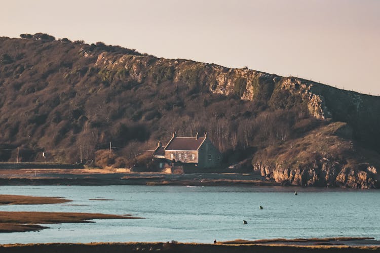 A Brown House Beside Brown Hill Near Body Of Water