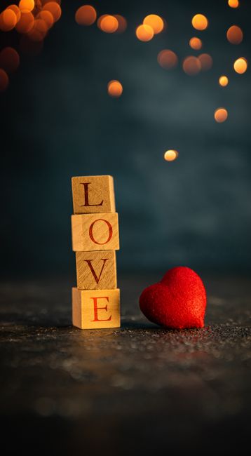 Fotomural Bloques de amor de madera y corazón rojo sobre un fondo oscuro con luces bokeh, perfecto para el tema de San Valentín.