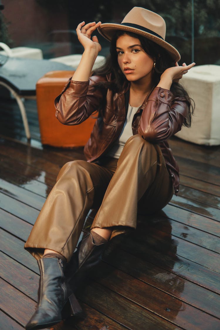 Woman In Brown Leather Jacket And Pants Sitting On Wooden Flooring 