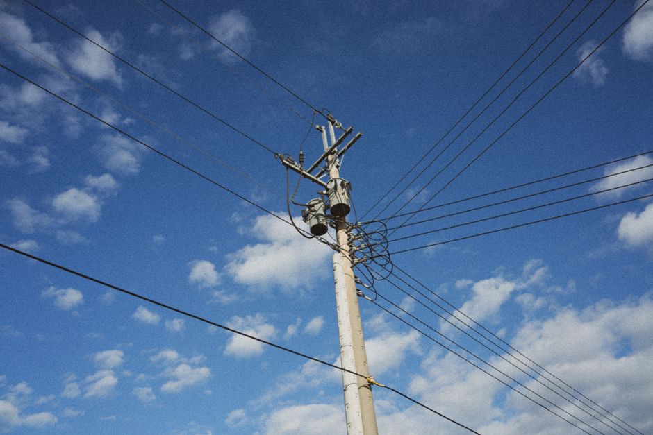 A utility pole with electrical lines stretching across a bright blue sky with scattered clouds.