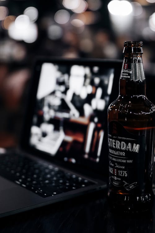 Free A Beer Bottle Beside a Laptop Stock Photo