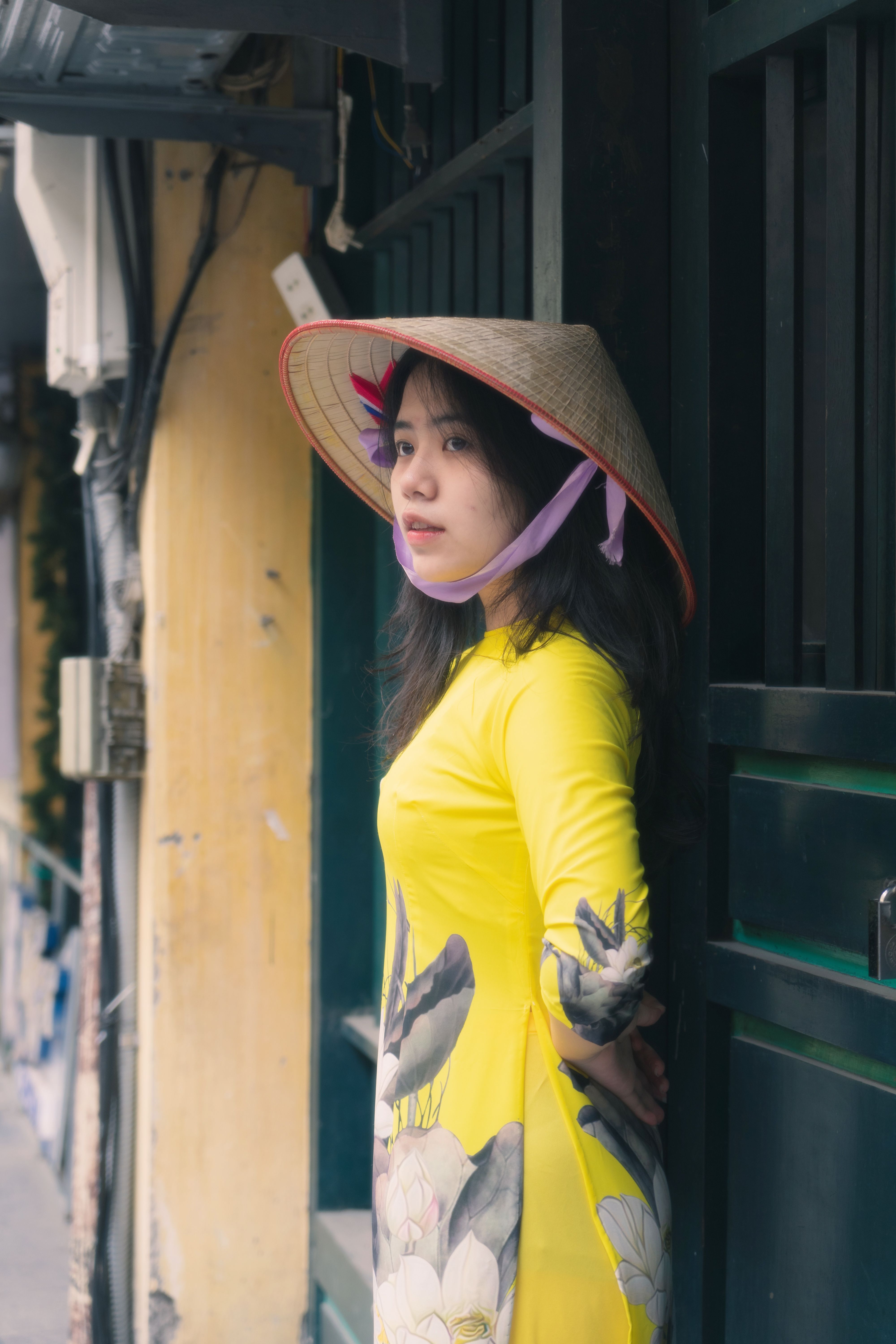 Woman in yellow dress and conical hat standing outdoors in Vietnam.