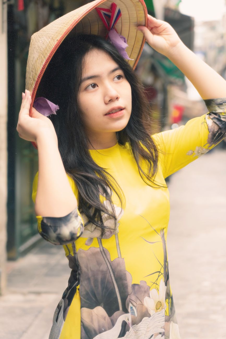 A young Vietnamese woman wearing ao dai and conical hat in a vibrant street scene.