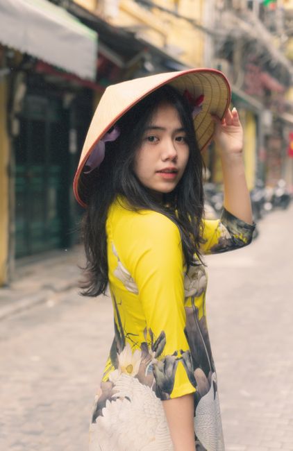 A young Vietnamese woman wearing traditional Ao Dai and a conical hat on a charming street in Vietnam.