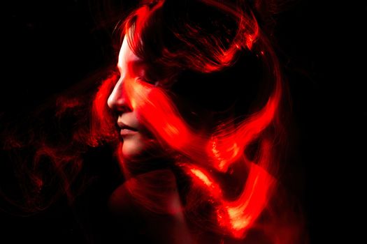 Artistic portrait featuring red light trails swirling around a woman's face against a dark background.