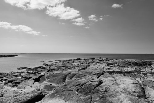 Free Black and white seashore image highlighting rocky terrain and cloudy sky, creating a serene scene. Stock Photo