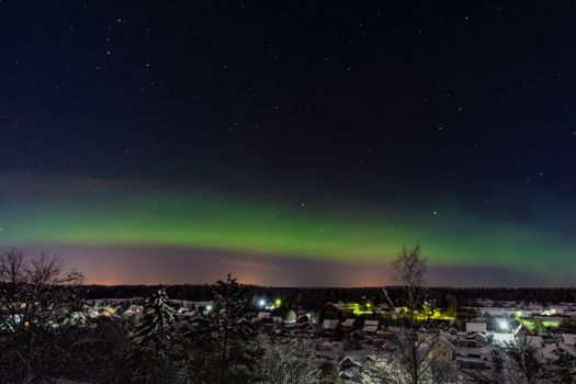 A breathtaking view of the northern lights over a snow-covered rural village at night.
