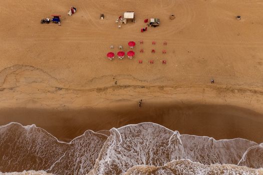 Aerial view of a sandy beach in Brazil with red umbrellas, chairs, and shoreline.