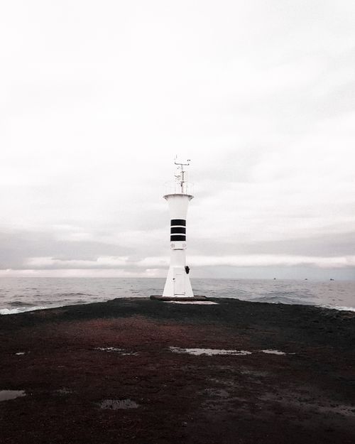 Free Serene scene of a solitary lighthouse by the sea under a cloudy sky. Stock Photo