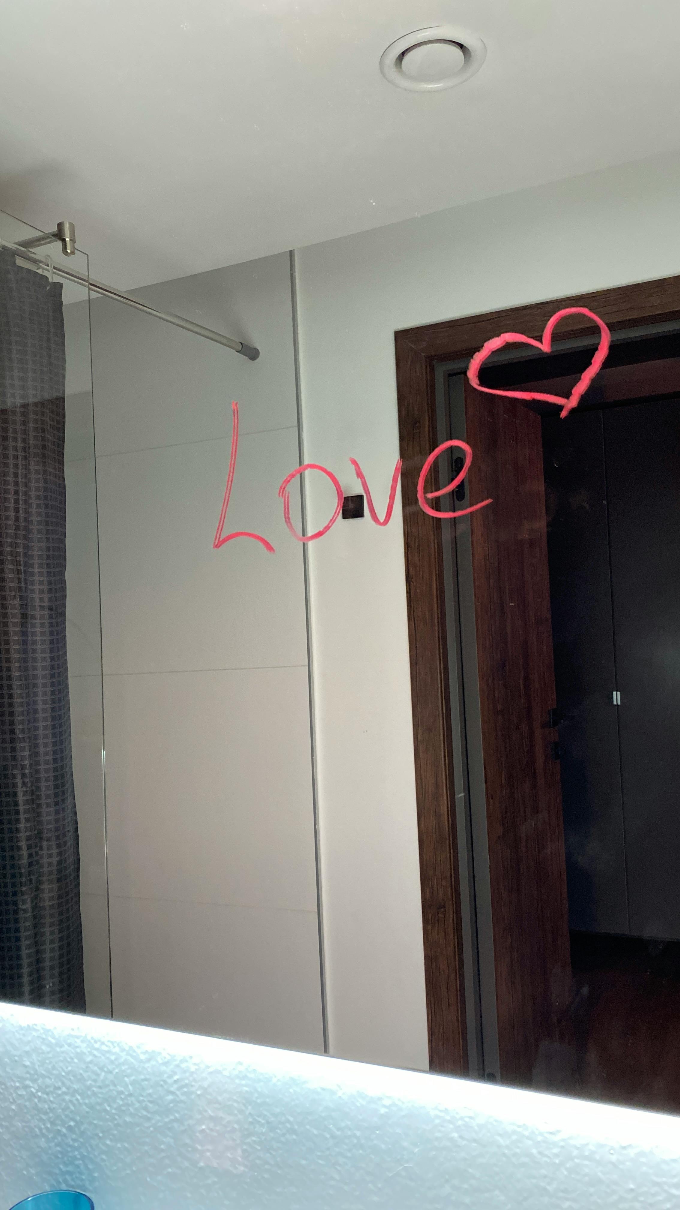 Reflection in a bathroom mirror with 'Love' and a heart written in red lipstick. A cozy modern setting.