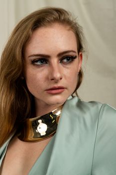 Close-up portrait of a woman in a stylish outfit with bold makeup and a gold necklace.