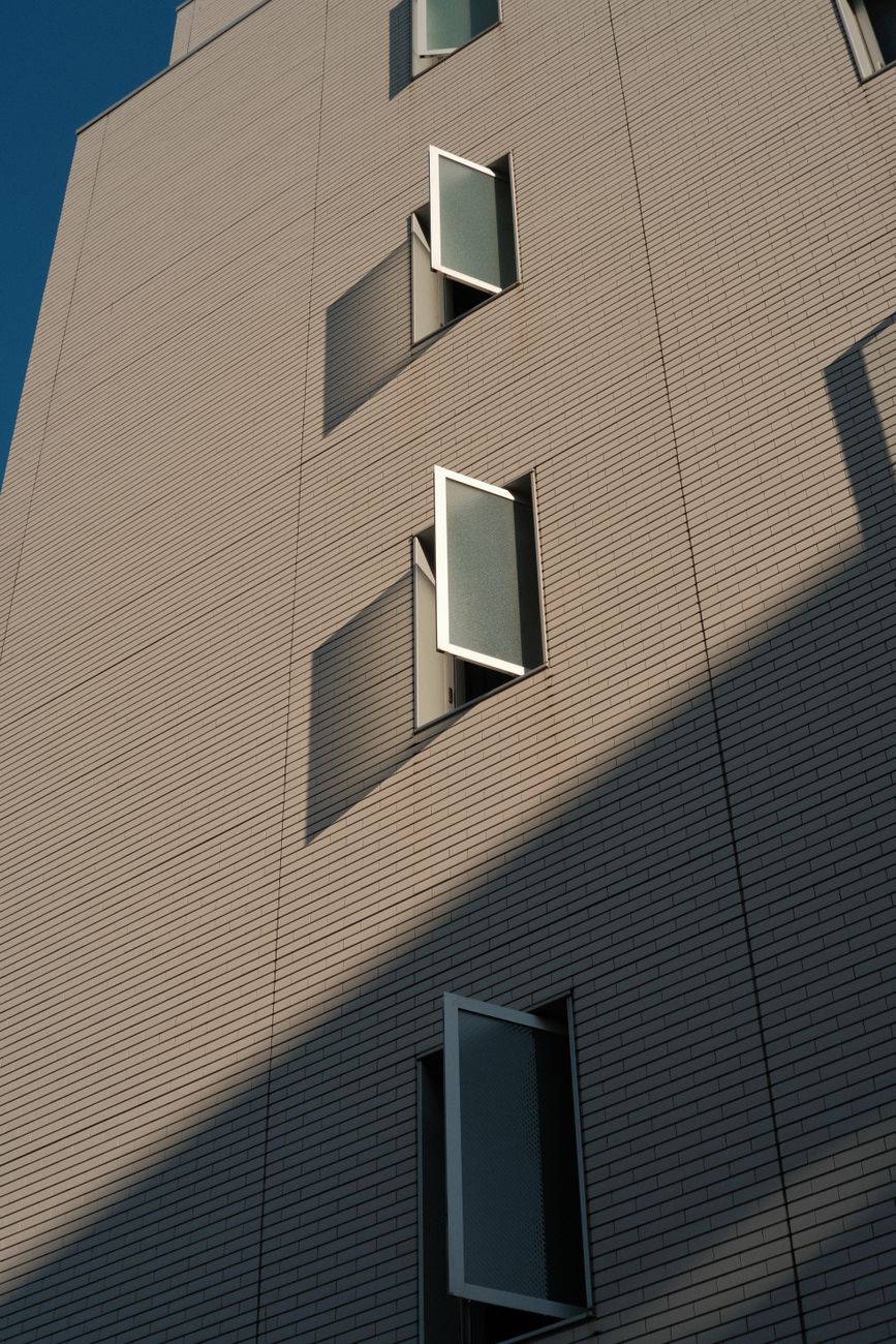 Vertical view of a modern building facade with several open windows casting shadows.