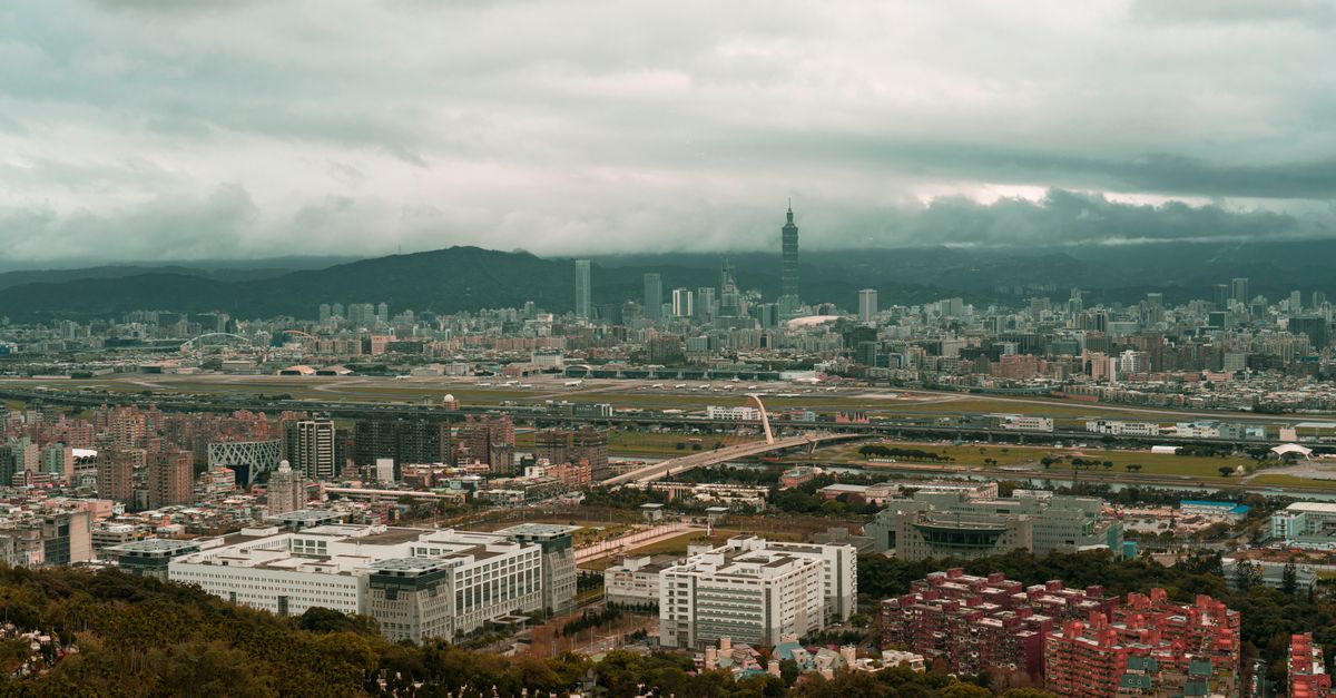 Dramatic aerial cityscape of Taipei under a moody sky, capturing urban sprawl and iconic architecture.