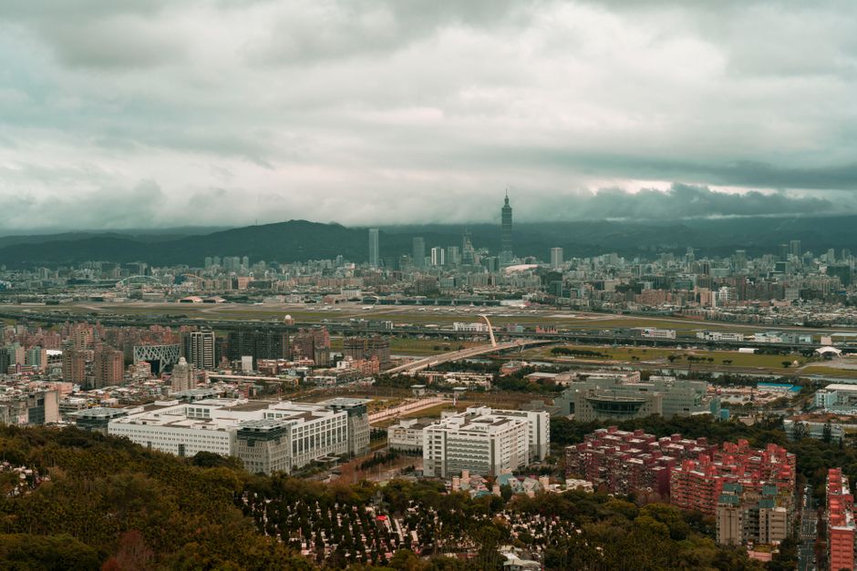 Dramatic aerial cityscape of Taipei under a moody sky, capturing urban sprawl and iconic architecture.