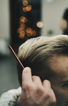 A man uses a comb to style his short blonde hair indoors.
