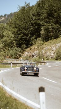 Classic vintage car driving on a curvy road with lush green forest backdrop, capturing a serene travel moment.