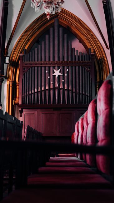 Majestic view of a church interior with ornate pipe organ architecture and red pews.