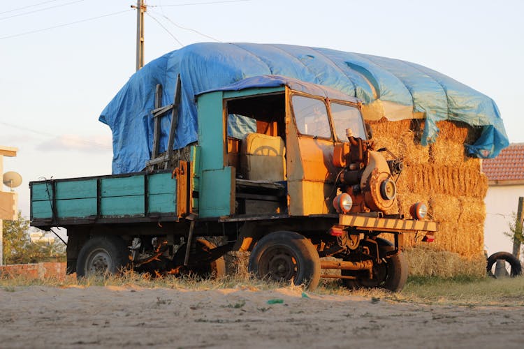 A Yellow Equipment On Old Truck Beside A Stack Of Hay