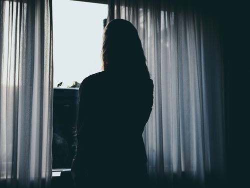 Free Silhouette of a woman standing by a window with flowing curtains, backlit by daylight. Stock Photo
