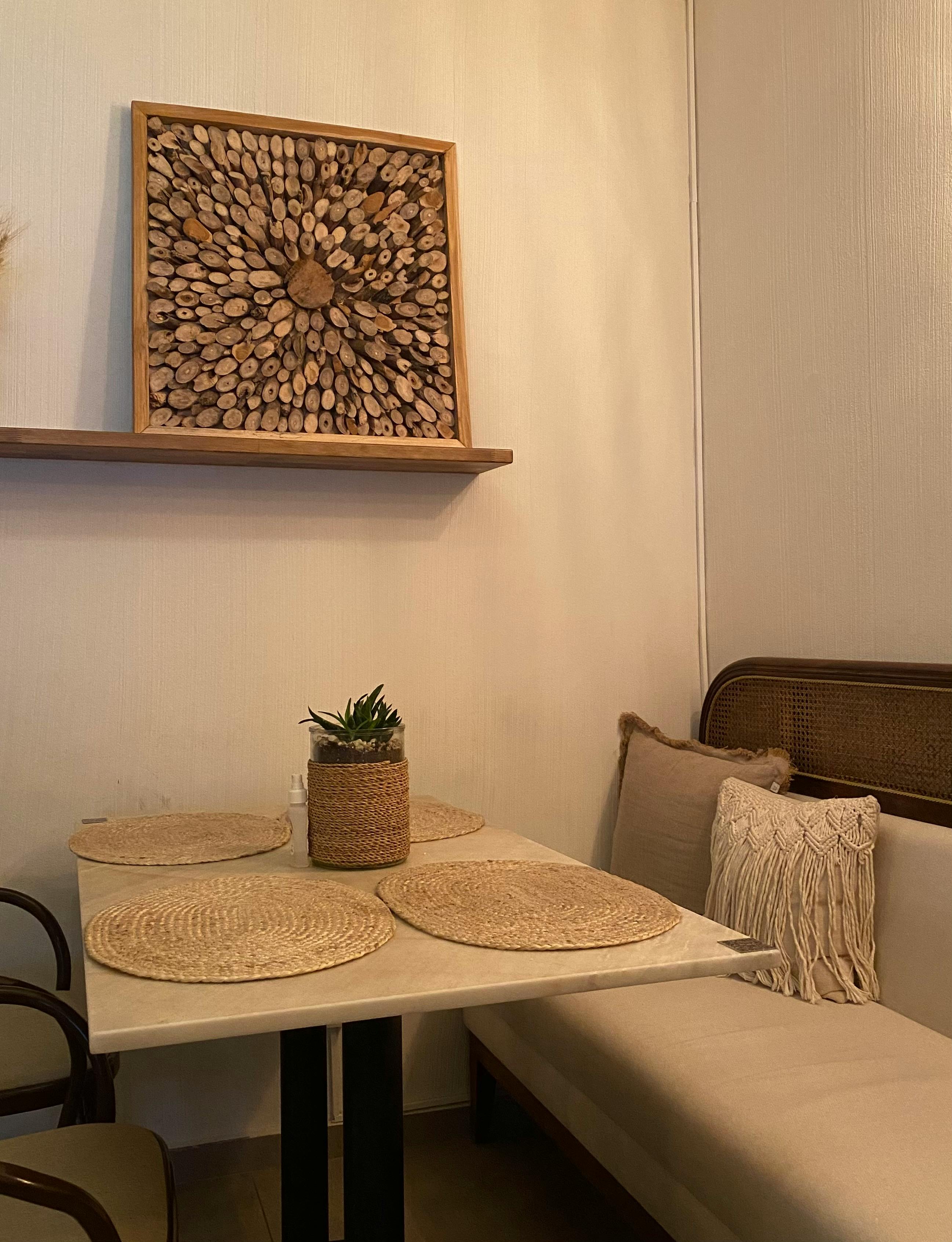 Free A small café corner featuring woven placemats, a rustic wooden artwork, and plush seating. Stock Photo