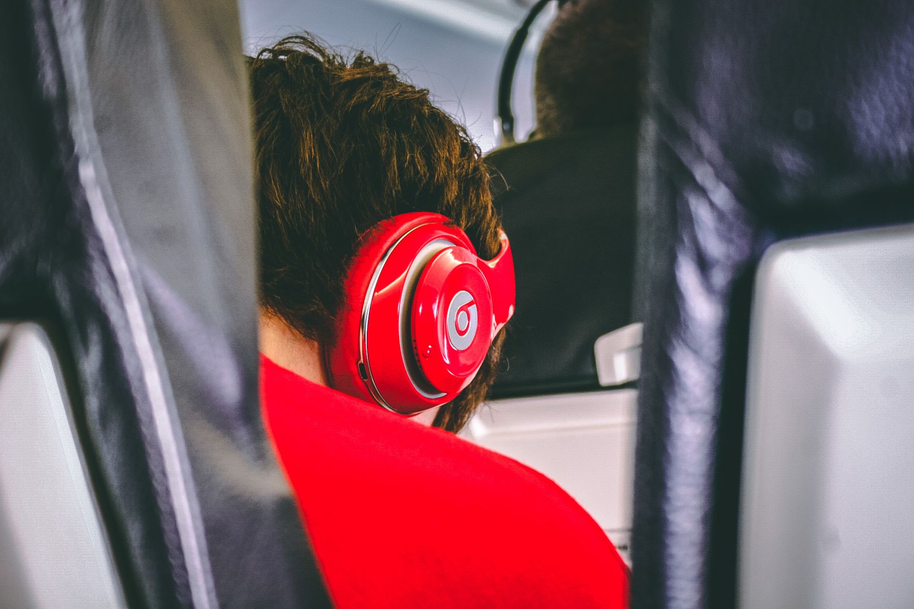 Teen wearing red headphones on an airplane, enjoying music during travel.