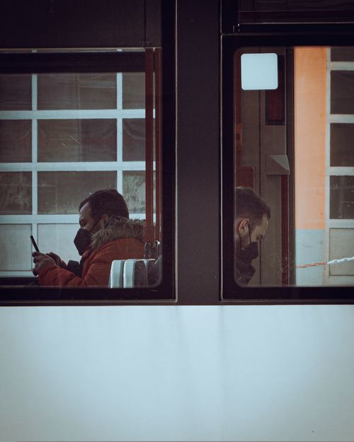 Free Two men wearing face masks sit inside a bus, focused on their phones during a daytime commute. Stock Photo