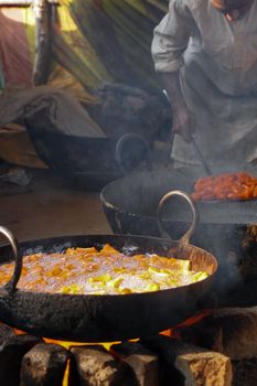 Close-up of traditional cooking with pans over open fire, showcasing vibrant ingredients.