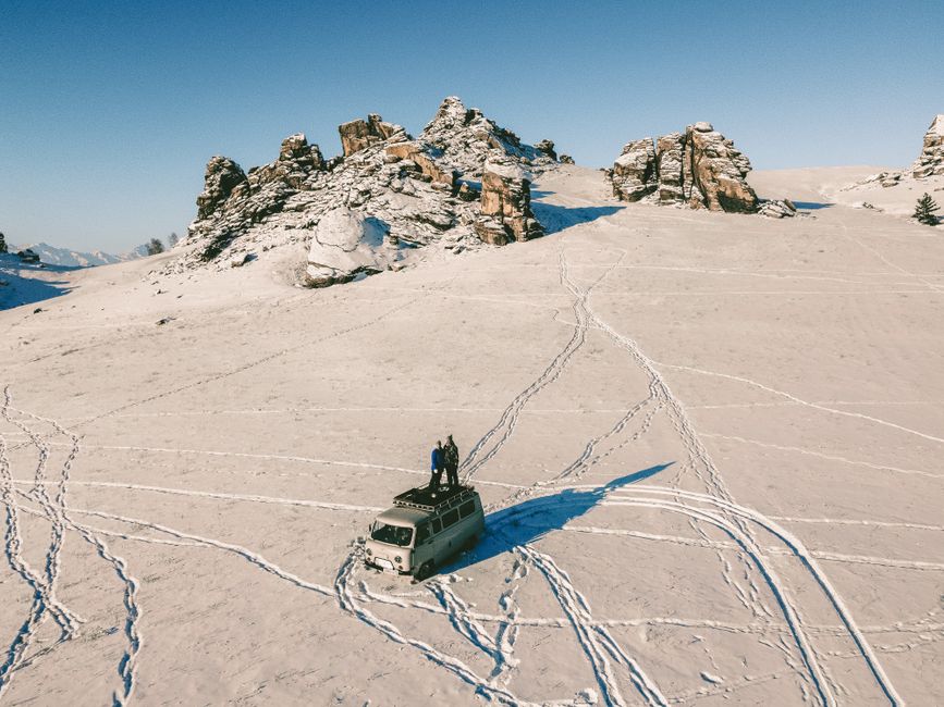 Drone captures people on a van amid a snow-covered mountain landscape in winter.