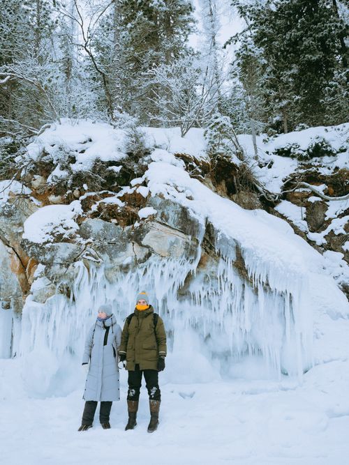 Free Couple standing amidst snowy landscape and ice formations, bundled in warm clothing. Winter adventure. Stock Photo