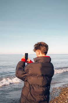 An individual in a black jacket photographs the ocean on a calm day in Turkey.