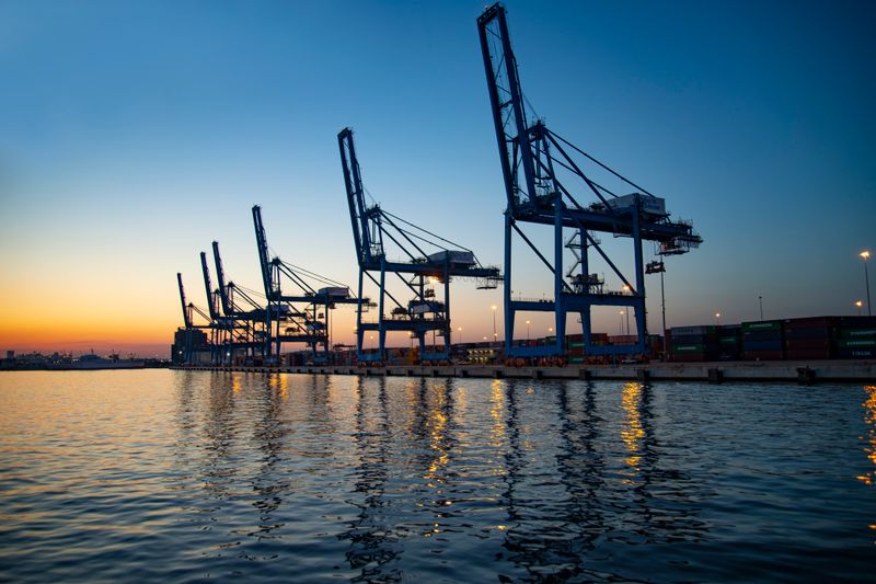Row of container gantry cranes along a port quay at dusk