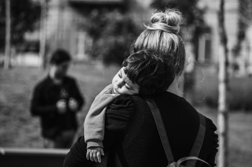 Free A serene black and white photo of a mother carrying her sleeping child outdoors. Stock Photo