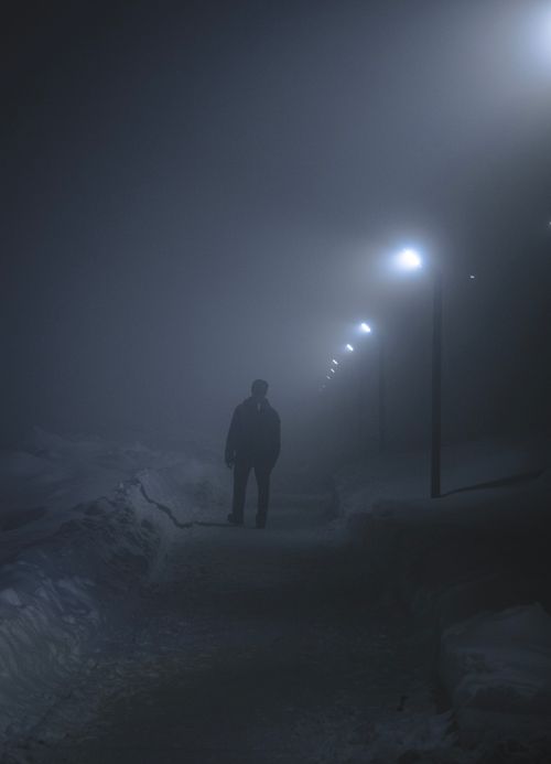 Free Silhouette of person walking under street lights in a foggy, misty night. Stock Photo