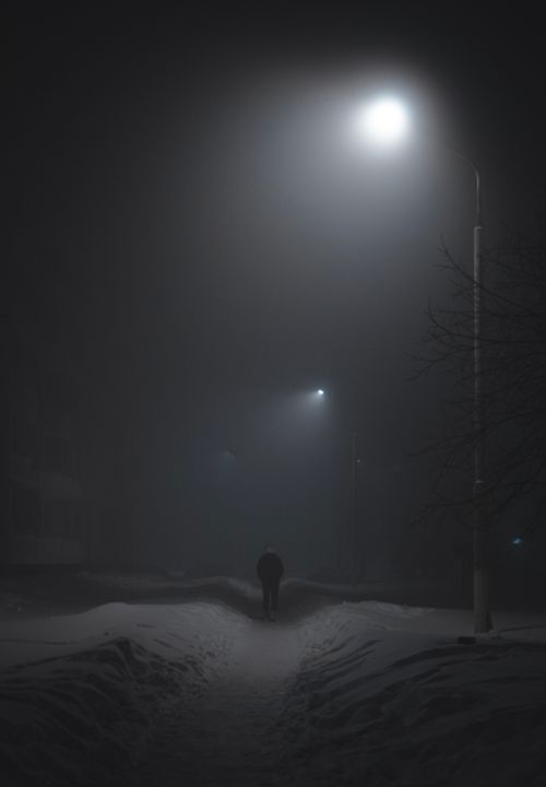 Free A lone figure walks down a foggy, snow-covered street at night under streetlights. Stock Photo