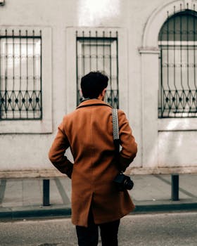 Man in brown coat with camera strolling down city street, capturing moments.