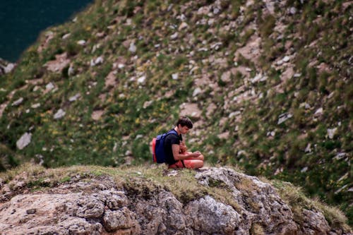 A Man Carrying Backpack Sitting on a Cliff