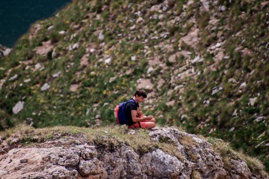 A man sits on a rocky mountain edge, enjoying solitude in nature.