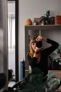 A female photographer takes a self portrait using a mirror in a stylish indoor setting.