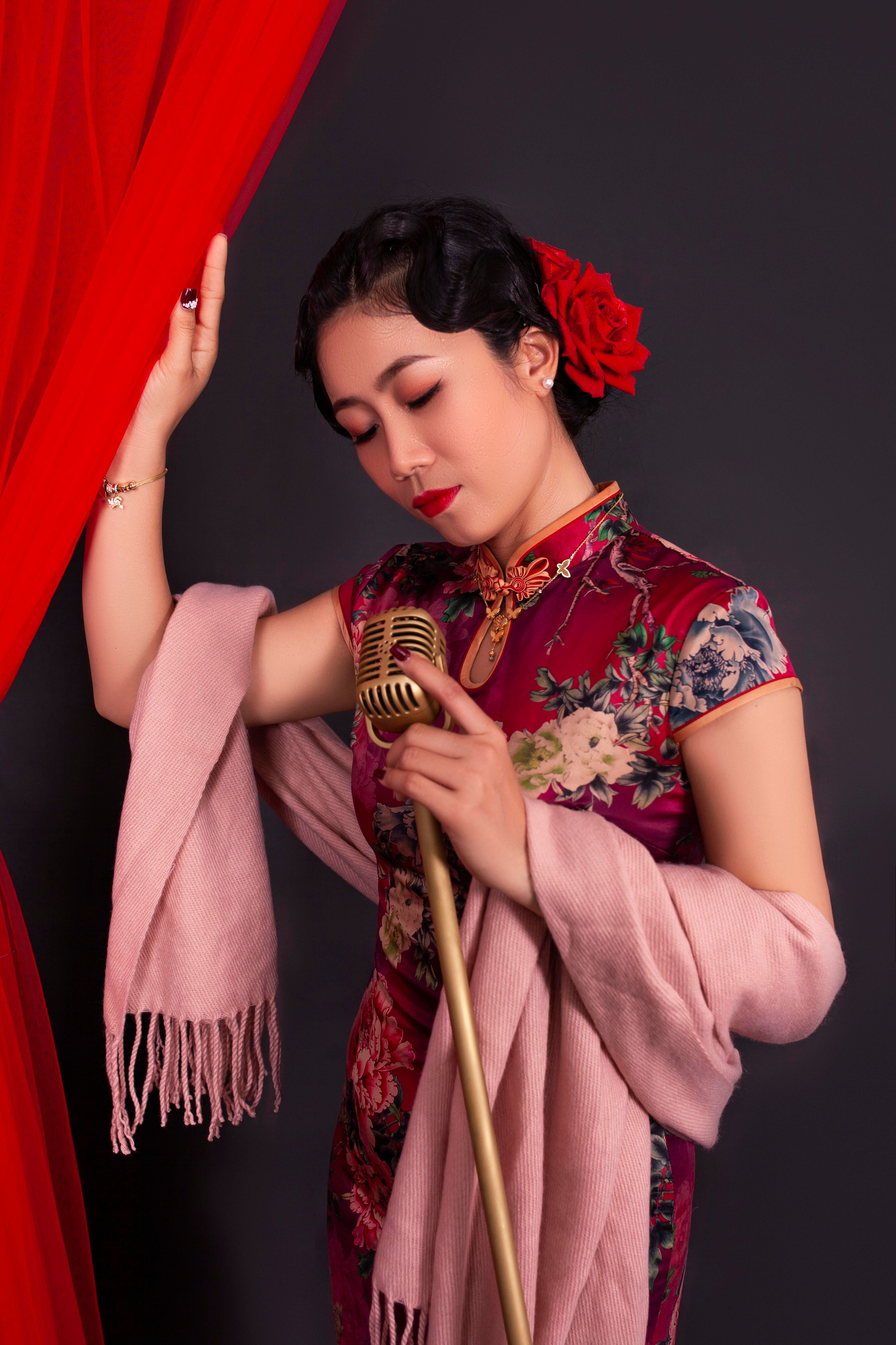 Asian woman in a qipao holding a vintage microphone, evoking a classic performance style.