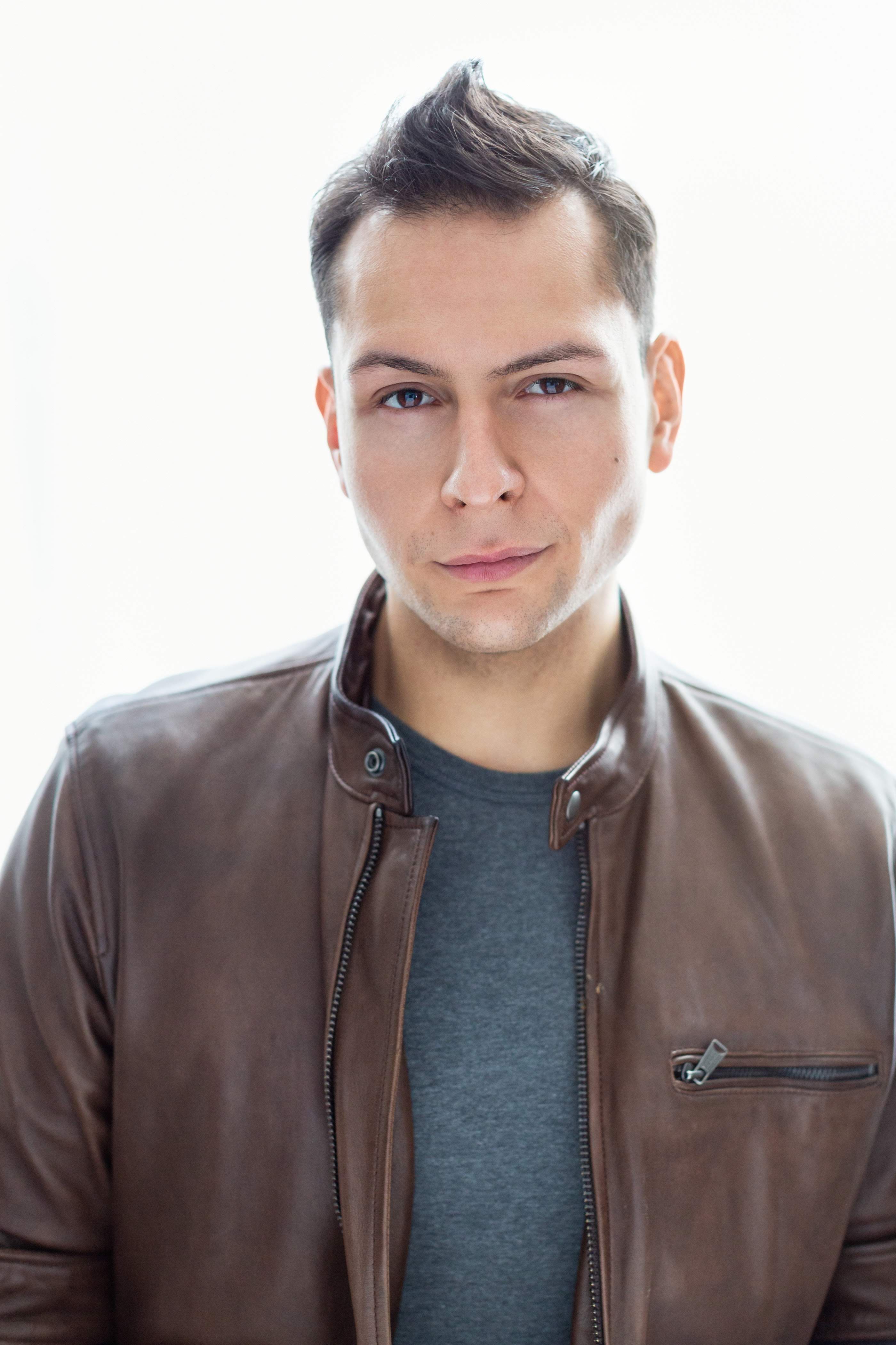 A serious portrait of a man wearing a brown leather jacket with a confident expression.
