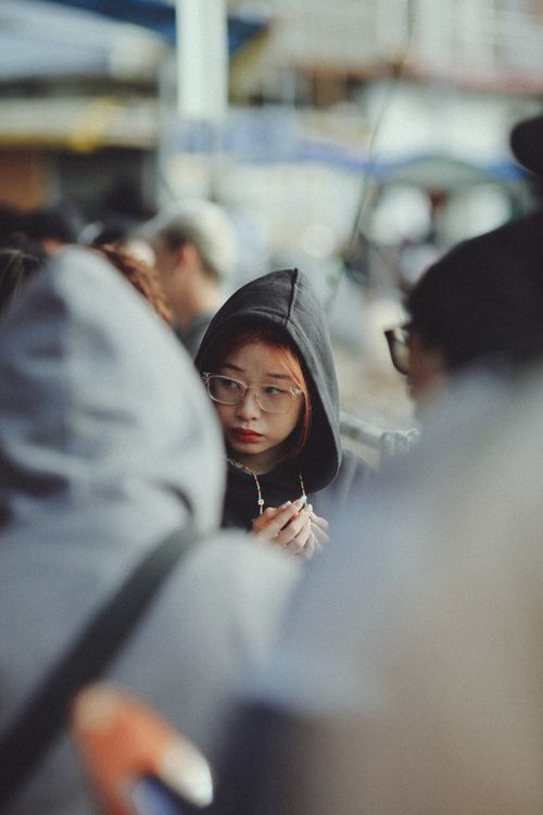 Free A young woman wearing glasses and a hoodie walks through a busy market street. Stock Photo