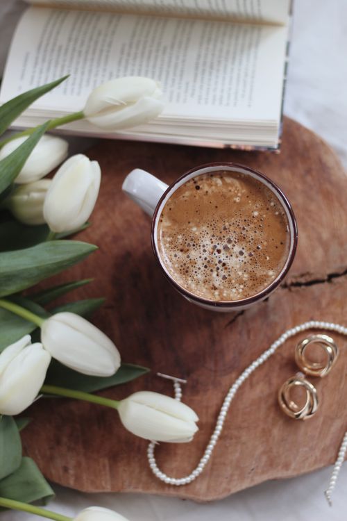 Free A cozy setting featuring a coffee cup, open book, white tulips, and jewelry on a wooden surface. Stock Photo