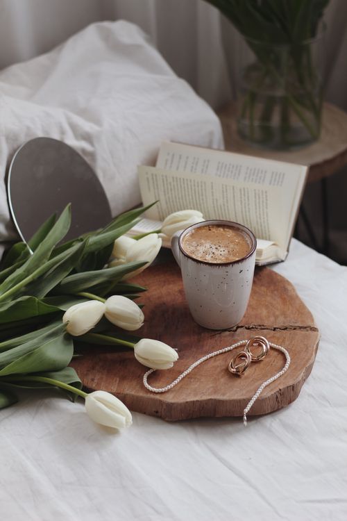 Free A cozy scene with a cup of coffee, book, tulips, and jewelry on a wooden tray. Stock Photo
