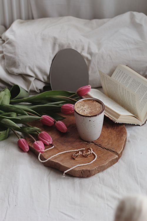 Free Relaxing morning setup with coffee, book, pink tulips, and jewelry on a bed. Stock Photo