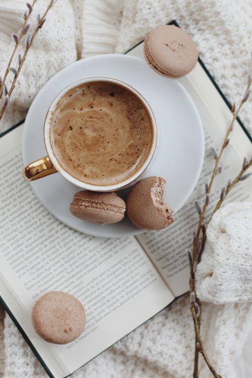 Free A comforting scene with coffee and macarons on an open book, surrounded by cozy textures. Stock Photo