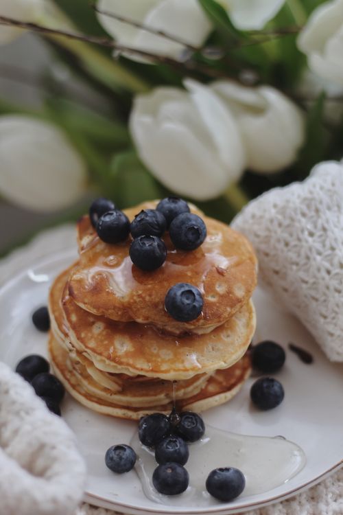 Free Stack of pancakes topped with blueberries and honey, surrounded by white flowers. Stock Photo