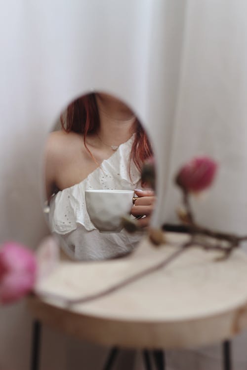 Mirror Reflection of a Woman Holding a Cup of Coffee