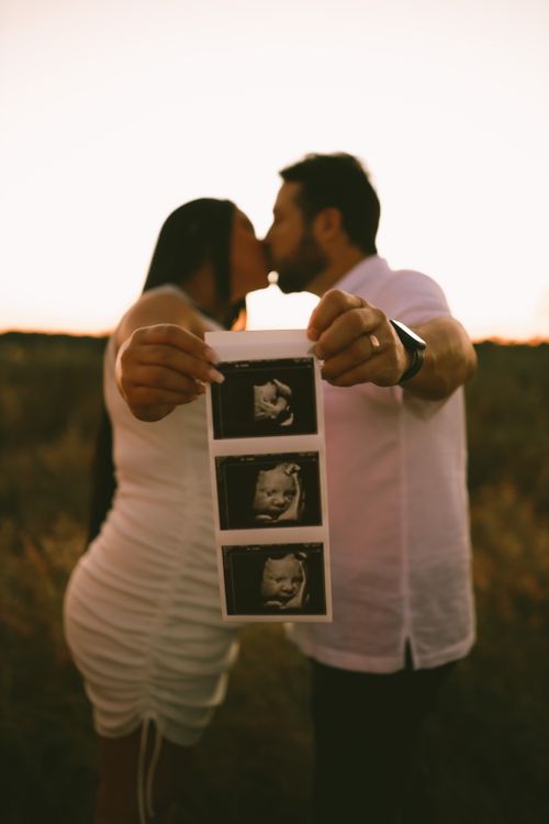 Free Pregnant couple kissing and holding ultrasound images outside. Stock Photo