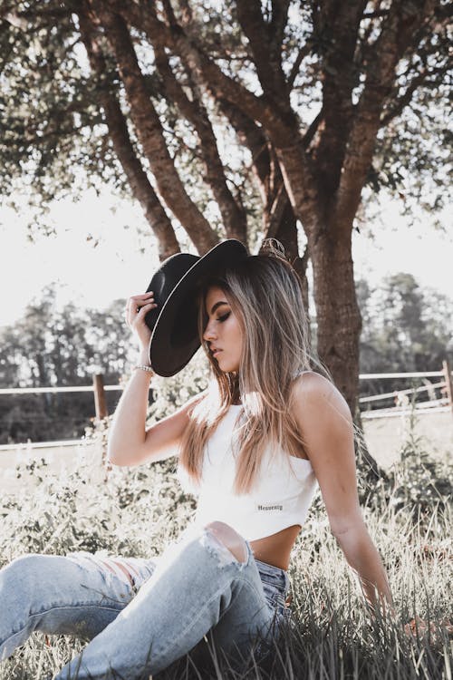 A Woman Holding her Hat While Sitting in the Grass